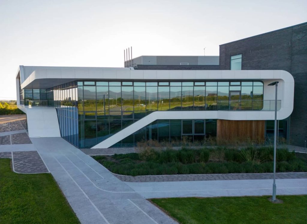 Modern building with large glass windows and white exterior, designed by an engineering consultancy, surrounded by walkways, grass, and landscaped greenery on a clear day.