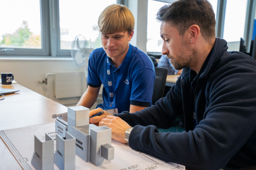 Two engineers looking at a 3D printed model of a mechanical layout on a desk